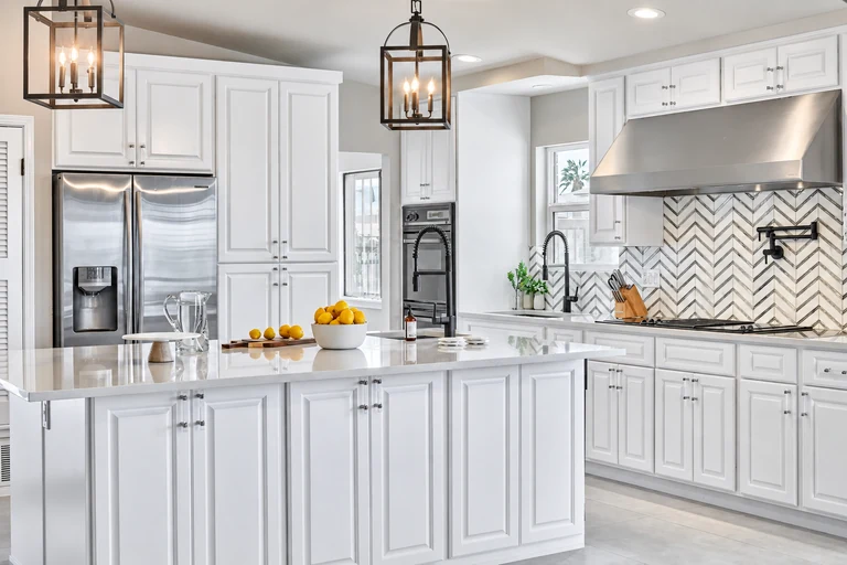 White kitchen with an island, stainless steel appliances, and a herringbone backsplash.